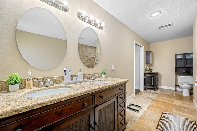 bathroom featuring a textured ceiling, visible vents, toilet, and a sink