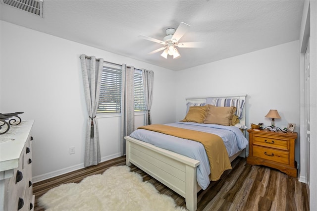bedroom featuring a ceiling fan, wood finished floors, a textured ceiling, baseboards, and visible vents