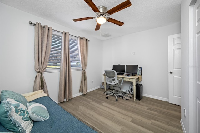 home office with wood finished floors, visible vents, a ceiling fan, baseboards, and a textured ceiling