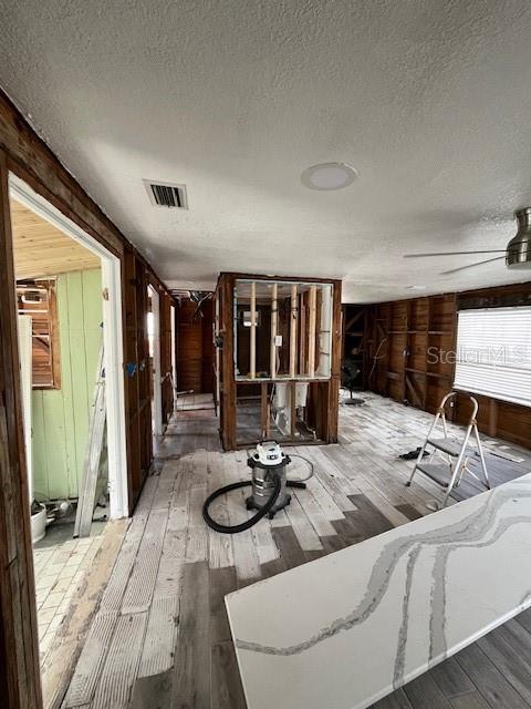 misc room featuring wood walls, hardwood / wood-style floors, ceiling fan, and a textured ceiling