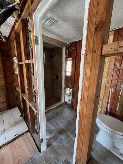 bathroom with a textured ceiling, toilet, and wooden walls