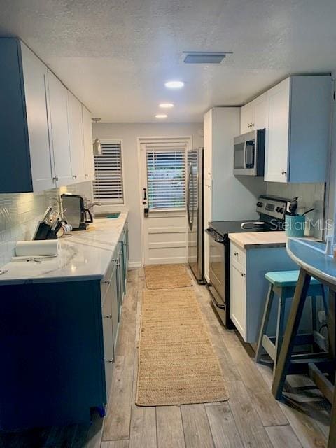 kitchen with appliances with stainless steel finishes, tasteful backsplash, a textured ceiling, sink, and white cabinetry