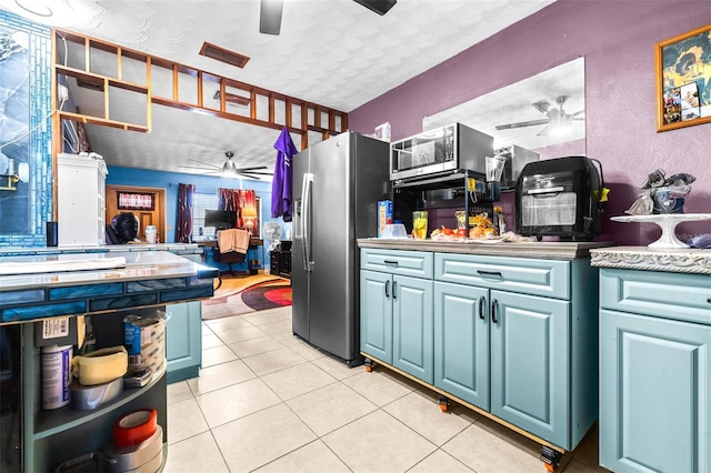 kitchen with appliances with stainless steel finishes, a textured ceiling, blue cabinets, and light tile patterned flooring