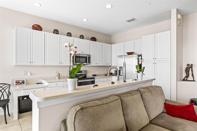 kitchen with appliances with stainless steel finishes, a center island with sink, white cabinetry, and light tile patterned flooring