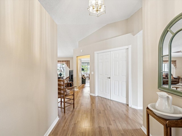 hall with light hardwood / wood-style floors, an inviting chandelier, and vaulted ceiling