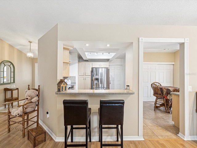 kitchen with kitchen peninsula, a kitchen breakfast bar, decorative light fixtures, stainless steel fridge with ice dispenser, and light hardwood / wood-style floors