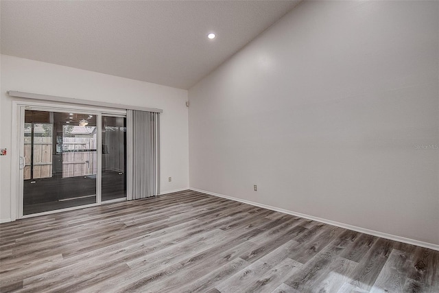 empty room with a textured ceiling, light hardwood / wood-style floors, and vaulted ceiling