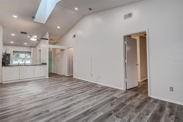 unfurnished living room with a skylight, ceiling fan, high vaulted ceiling, and hardwood / wood-style flooring