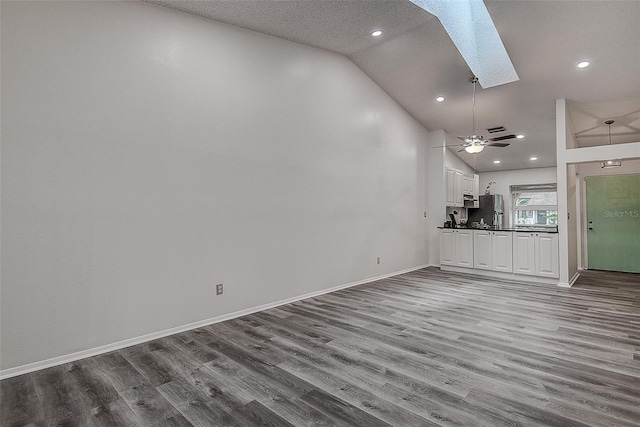 unfurnished living room featuring a textured ceiling, hardwood / wood-style flooring, ceiling fan, and vaulted ceiling with skylight