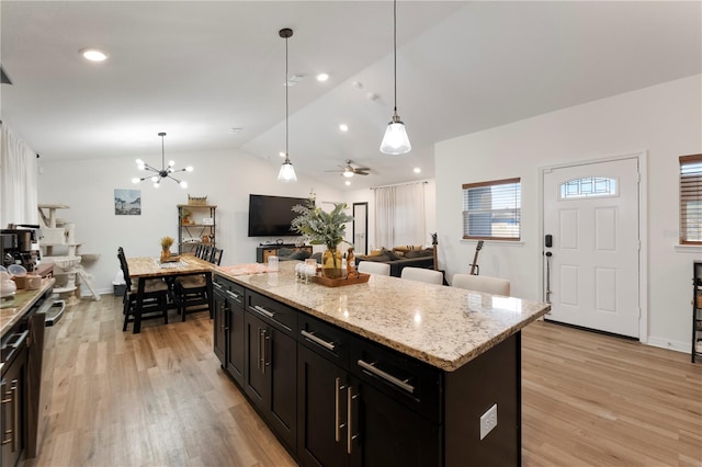 kitchen with a center island, lofted ceiling, hanging light fixtures, light stone counters, and light hardwood / wood-style flooring