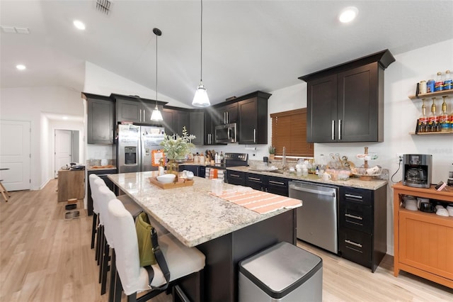 kitchen with vaulted ceiling, hanging light fixtures, appliances with stainless steel finishes, and a kitchen island