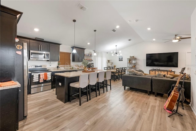 kitchen featuring decorative light fixtures, vaulted ceiling, a kitchen island, light hardwood / wood-style floors, and appliances with stainless steel finishes