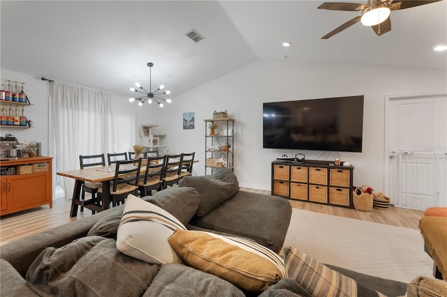 living room with vaulted ceiling, ceiling fan with notable chandelier, and light hardwood / wood-style flooring