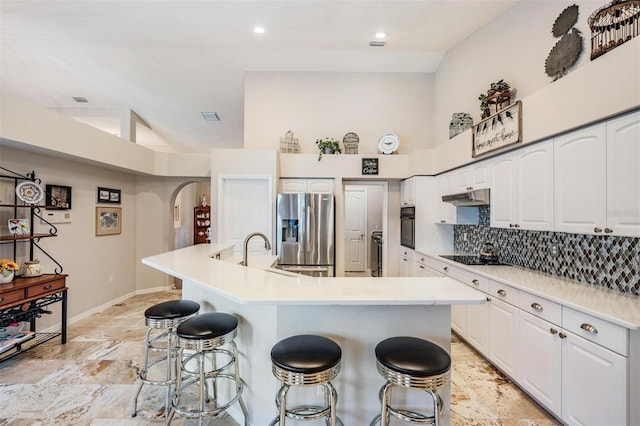 kitchen featuring a breakfast bar area, white cabinetry, a center island with sink, and black appliances