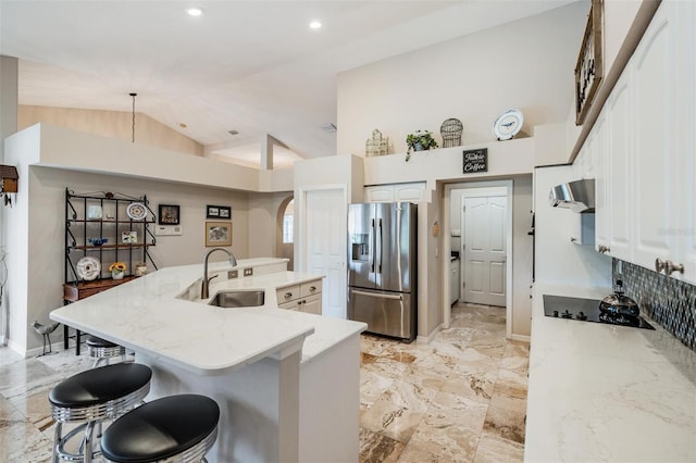 kitchen featuring hanging light fixtures, sink, stainless steel fridge, black electric cooktop, and a breakfast bar area