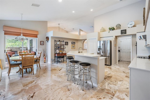 kitchen featuring a kitchen island with sink, white cabinets, a kitchen breakfast bar, decorative light fixtures, and stainless steel fridge with ice dispenser