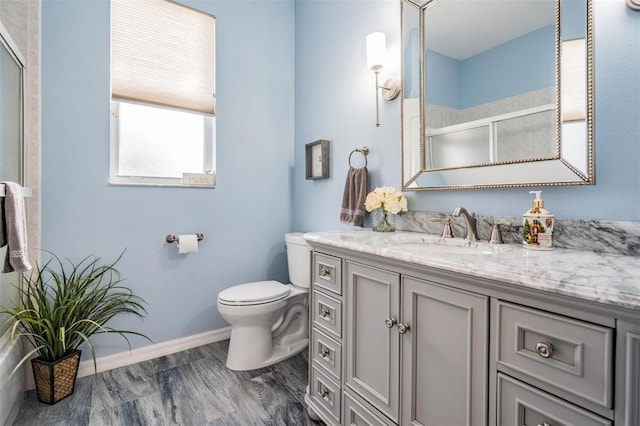 bathroom featuring wood-type flooring, vanity, toilet, and a shower with shower door