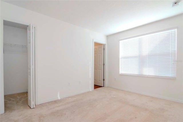 unfurnished bedroom with a spacious closet, light carpet, and a closet