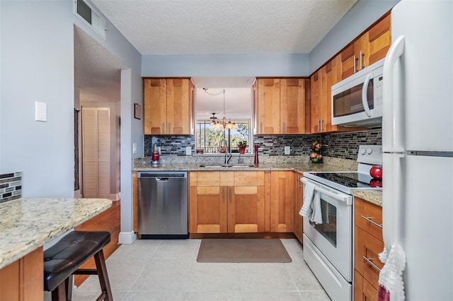 kitchen featuring light stone countertops, white appliances, sink, and an inviting chandelier