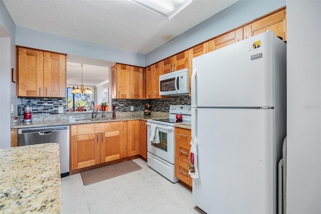 kitchen featuring white appliances, sink, light stone countertops, a textured ceiling, and a chandelier