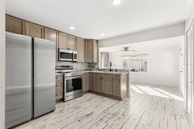 kitchen featuring sink, decorative backsplash, ceiling fan, appliances with stainless steel finishes, and kitchen peninsula