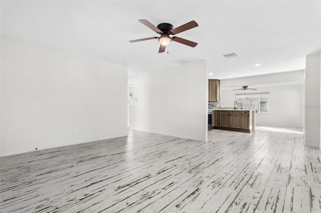 unfurnished living room featuring ceiling fan, sink, and light wood-type flooring