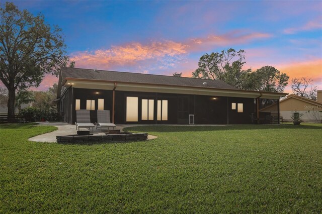 back house at dusk with a patio area and a lawn