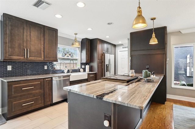 kitchen featuring sink, hanging light fixtures, appliances with stainless steel finishes, dark brown cabinets, and light stone counters