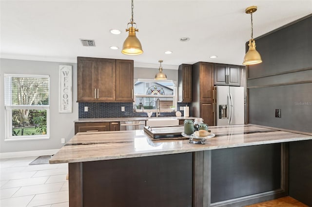 kitchen featuring light stone countertops, decorative light fixtures, dark brown cabinets, appliances with stainless steel finishes, and ornamental molding