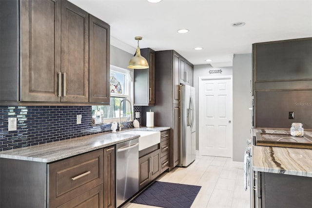 kitchen featuring appliances with stainless steel finishes, light stone counters, dark brown cabinets, sink, and hanging light fixtures