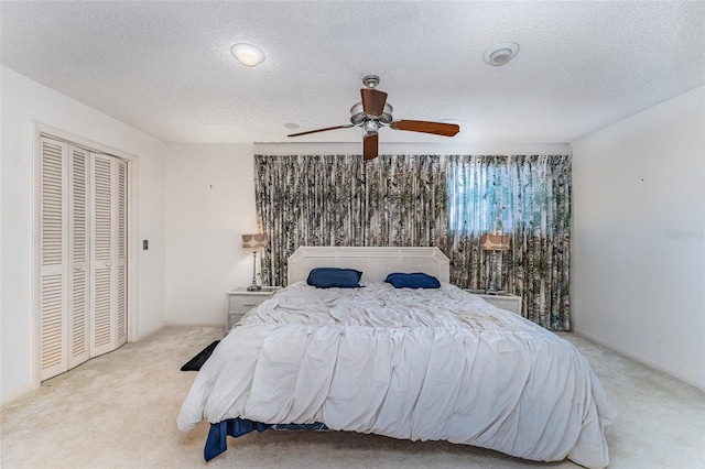 bedroom with ceiling fan, light colored carpet, a closet, and a textured ceiling