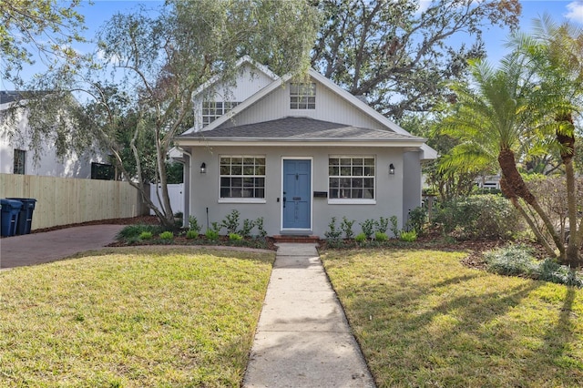 bungalow-style home featuring stucco siding, fence, a front yard, and roof with shingles