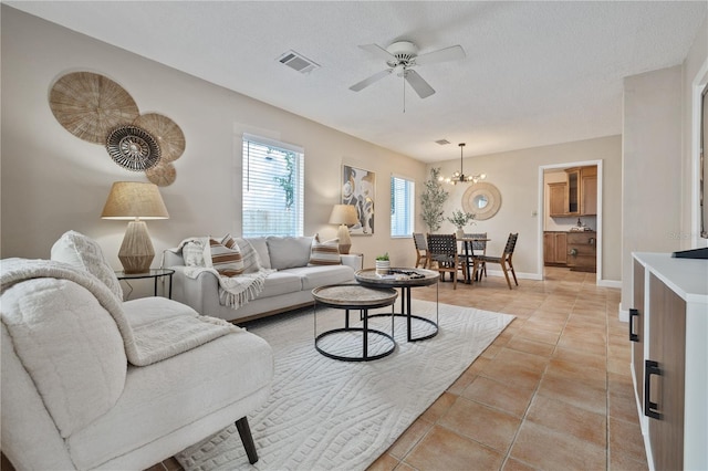 living room featuring light tile patterned floors, ceiling fan with notable chandelier, and a textured ceiling