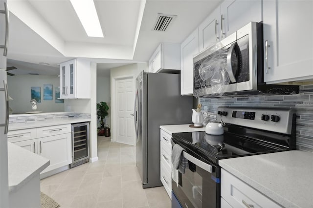 kitchen with light tile patterned floors, wine cooler, decorative backsplash, white cabinets, and appliances with stainless steel finishes