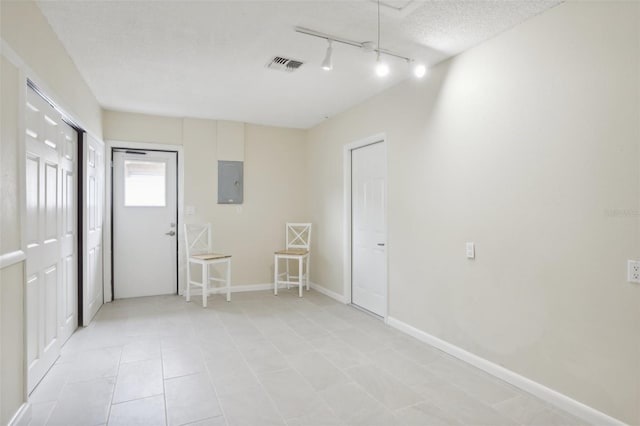 unfurnished room featuring a textured ceiling, electric panel, light tile patterned flooring, and track lighting