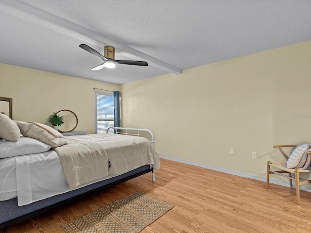 bedroom with ceiling fan, beam ceiling, a textured ceiling, and light hardwood / wood-style flooring