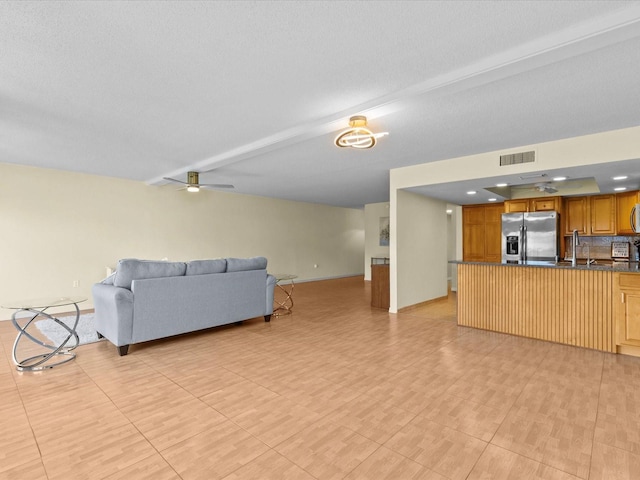 living room featuring beam ceiling, ceiling fan, sink, and a textured ceiling