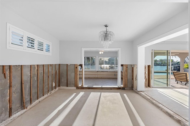 spare room with ceiling fan with notable chandelier and a water view