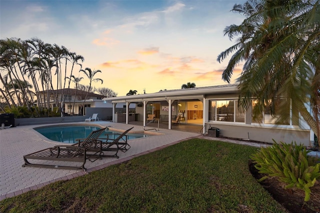 pool at dusk featuring a patio area and a yard