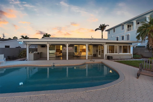 pool at dusk with an outdoor kitchen and a patio