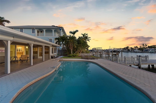 pool at dusk featuring a patio, a dock, and a water view