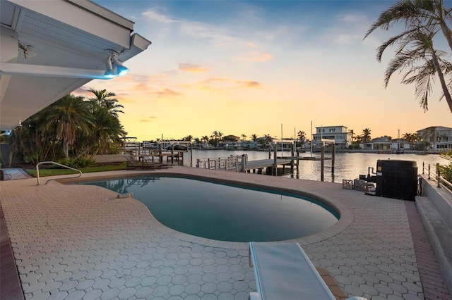 pool at dusk with a dock, a patio, and a water view