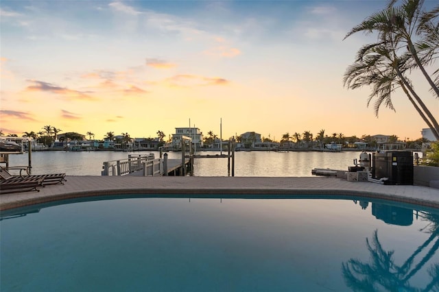 pool at dusk featuring a boat dock and a water view