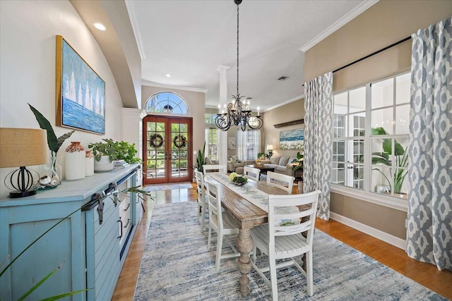 dining space featuring a chandelier, light wood-type flooring, crown molding, and french doors