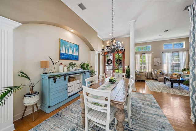 dining space featuring an inviting chandelier, wood-type flooring, ornamental molding, and ornate columns