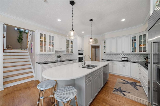 kitchen with sink, backsplash, decorative light fixtures, a kitchen island with sink, and white cabinets