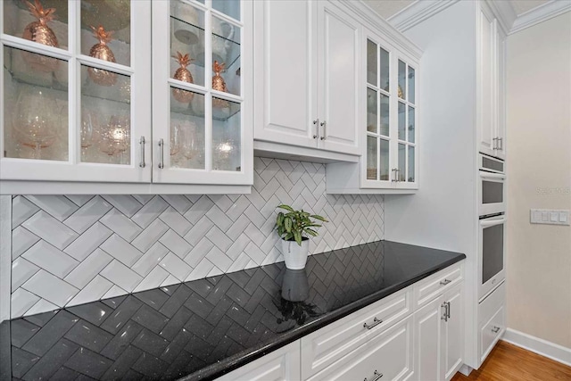 kitchen with decorative backsplash, ornamental molding, double oven, light hardwood / wood-style floors, and white cabinetry