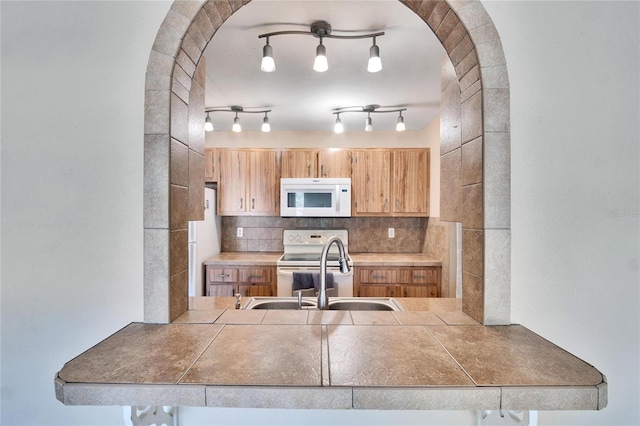 kitchen featuring tile countertops, decorative backsplash, white appliances, and sink