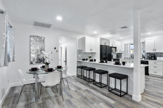 kitchen featuring a breakfast bar, black appliances, kitchen peninsula, light hardwood / wood-style floors, and white cabinetry