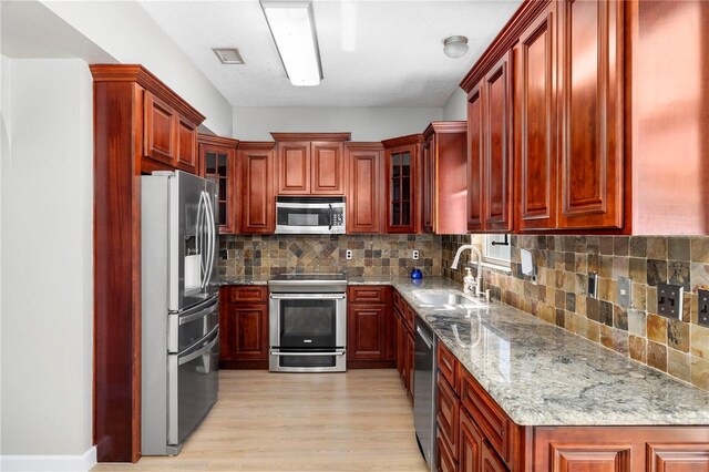 1600 Gray Bark Dr, Oldsmar, FL 34677 - kitchen with reddish brown cabinets, light stone counters, a sink, light wood-style flooring, and appliances with stainless steel finishes